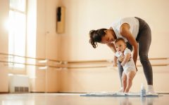Young happy mother teaching her baby to stand in a health club.